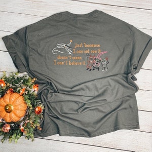 Puede incluir: Una camiseta verde oscuro con un dise&ntilde;o bordado con personajes de la pel&iacute;cula "Pesadilla antes de Navidad". El texto dice "Solo porque no pueda verlo no significa que no pueda creerlo."