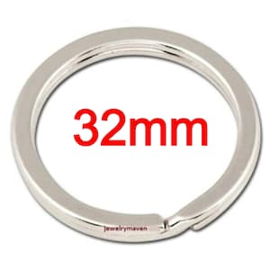 May include: A circular silver-toned metal split ring for keys with a flat profile. The ring features a clearly printed measurement of 32mm in red text across the center. The metal surface has a smooth, reflective finish and a standard coil design.