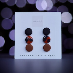 May include: Three pairs of stud earrings displayed on a white card. The earrings are black, brown, and a mottled brown and black pattern. The card reads "Molly & Mouse" and "Handmade in Scotland".