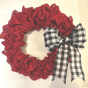 May include: A red burlap wreath with a large black and white checkered bow. The bow is tied in a knot and the tails are long and flowing.