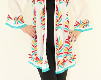 May include: White embroidered kimono with red, yellow, and blue floral designs. The kimono has a lace trim and is worn over a black top and black leggings.