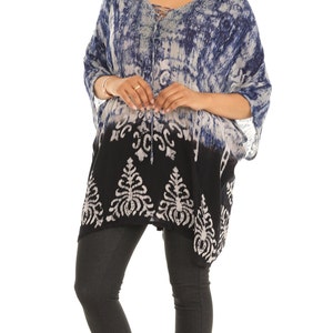 May include: A blue and white tie-dye tunic with a black and white patterned bottom. The tunic has a V-neck and a drawstring closure. The model is wearing black leggings and white shoes.