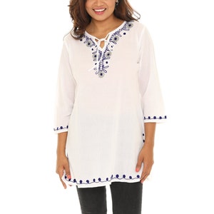 May include: White cotton tunic top with a blue embroidered floral design around the neckline and a tie at the neck. The top has blue embroidered trim around the hem and sleeves.