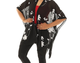 May include: Black floral embroidered kimono-style cover-up. The sheer fabric features white floral embroidery. The cover-up is worn over a red top and black pants. White sandals with flower accents complete the outfit.