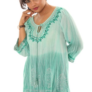 May include: A teal blue, semi-sheer, embroidered top with a tie at the neckline and a tassel at the bottom. The top has a tie at the neckline and a tassel at the bottom.