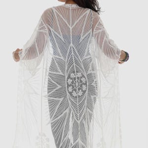 May include: A white, sheer, long-sleeved kimono with an intricate floral and geometric lace design. The open-front cardigan features a detailed pattern on the back and sleeves, with a scalloped lace trim along the bottom edge. A stylish, lightweight cover-up.