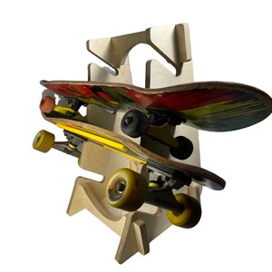 Puede incluir: Un soporte de madera para skateboards con dos skateboards. El skateboard superior tiene un dise&ntilde;o rojo, amarillo y verde. El skateboard inferior tiene un dise&ntilde;o amarillo y negro.