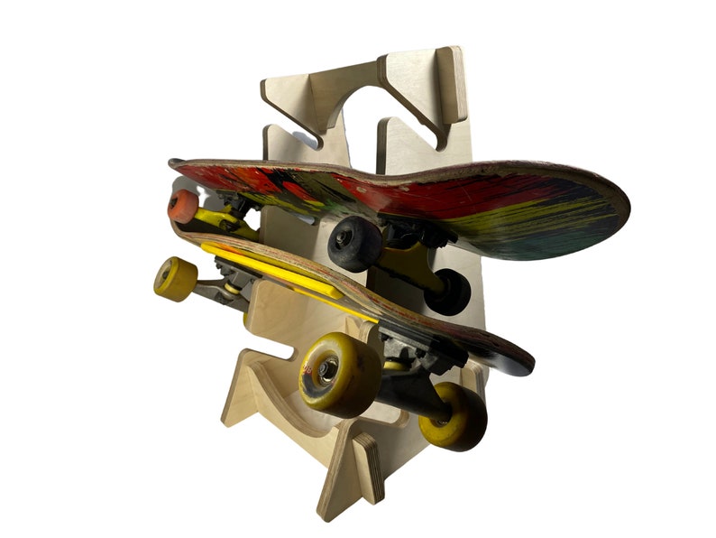 Puede incluir: Un soporte de madera para skateboards con dos skateboards. El skateboard superior tiene un dise&ntilde;o rojo, amarillo y verde. El skateboard inferior tiene un dise&ntilde;o amarillo y negro.