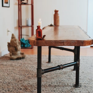 May include: A wooden table with a live edge top and black metal pipe legs. A small candle is burning in a glass bottle on the table.