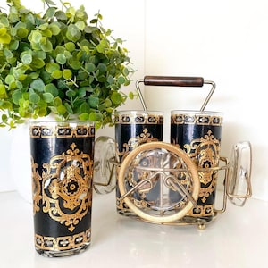 Parchemin MCM vintage en or 22 carats sur des verres à whisky noirs dans un support en métal MCM