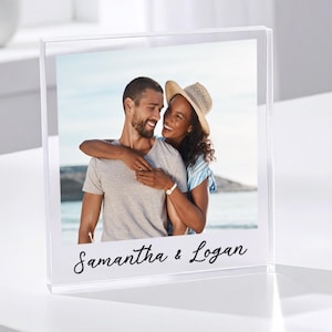 May include: A clear acrylic photo block displaying a color photograph of a smiling couple embracing. The photo is bordered in white, with the names "Samantha & Logan" in script at the bottom. The block is on a white surface.