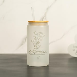 May include: A frosted glass tumbler with a bamboo lid and a straw. The tumbler has a floral design and the name "Madison" engraved on it.