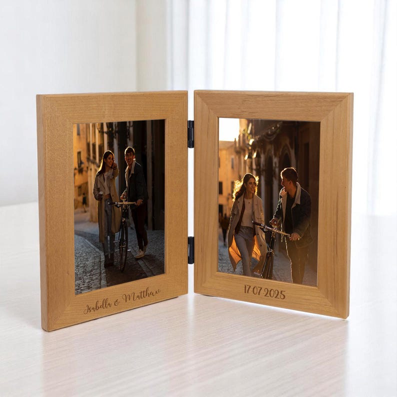 May include: A hinged, light-colored wooden photo frame with two panels. Each panel holds a photograph of a couple. The left panel is inscribed with "Isabella & Matthew", and the right panel has the date "17 07 2025".