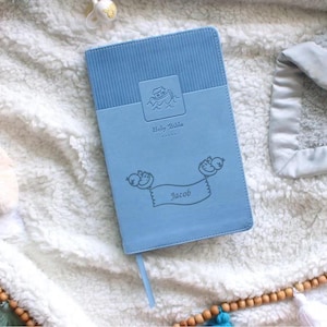 Pu&ograve; includere: Una Bibbia personalizzata blu chiaro con un piccolo grafico di una barca e il nome Jacob su uno stendardo tenuto da due uccelli.