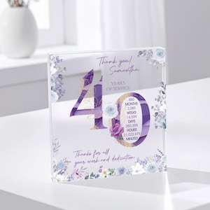 May include: A clear acrylic block with a purple and gold design, celebrating 40 years of service. The block features floral accents, the text "Thank you! Samantha," and a breakdown of service time in months, weeks, days, hours, and minutes.