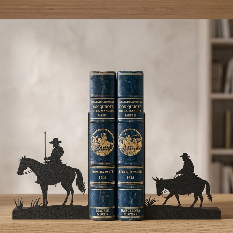 Puede incluir: Dos libros de tapa dura azul oscuro titulados Don Quijote de la Mancha, Parte I y Parte II, est&aacute;n sujetos por dos sujetalibros de metal negro. El sujetalibros izquierdo muestra la silueta de un jinete a caballo, y el derecho un jinete sobre un burro.