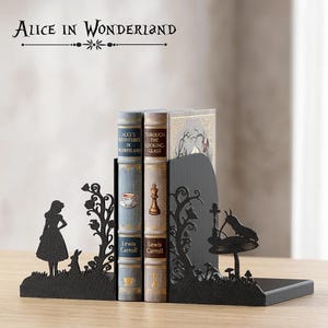 Può includere: Reggilibri in metallo nero con sagome di Alice nel Paese delle Meraviglie. Sostengono tre libri, tra cui "Alice's Adventures in Wonderland" e "Through the Looking-Glass" di Lewis Carroll. Il testo "Alice in Wonderland" è sopra.