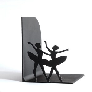 May include: Black metal bookends featuring silhouettes of two ballerinas in graceful poses. The bookends have a flat base and a vertical support, perfect for organizing books on a shelf or desk. The design adds a touch of elegance to any space.