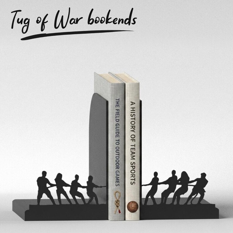 Puede incluir: Sujetalibros de metal negro con dise&ntilde;o de tira y afloja. Los sujetalibros sostienen dos libros, "The Field Guide to Outdoor Games" y "A History of Team Sports." El texto "Tug of War bookends" est&aacute; escrito encima.