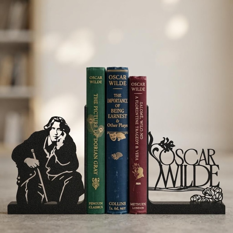 Puede incluir: Un juego de sujetalibros de metal negro con la silueta de Oscar Wilde en un lado y el texto Oscar Wilde con detalles florales en el otro, sosteniendo tres libros titulados The Picture of Dorian Gray, The Importance of Being Earnest y Salome.