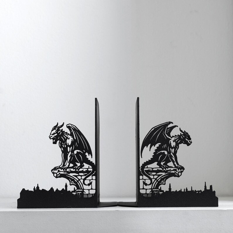 Puede incluir: Sujetalibros de metal negro con un dise&ntilde;o de g&aacute;rgola g&oacute;tica. Cada sujetalibros representa una criatura alada posada sobre una repisa decorativa con una base de horizonte urbano. Los sujetalibros est&aacute;n dise&ntilde;ados para sostener libros en posici&oacute;n vertical.