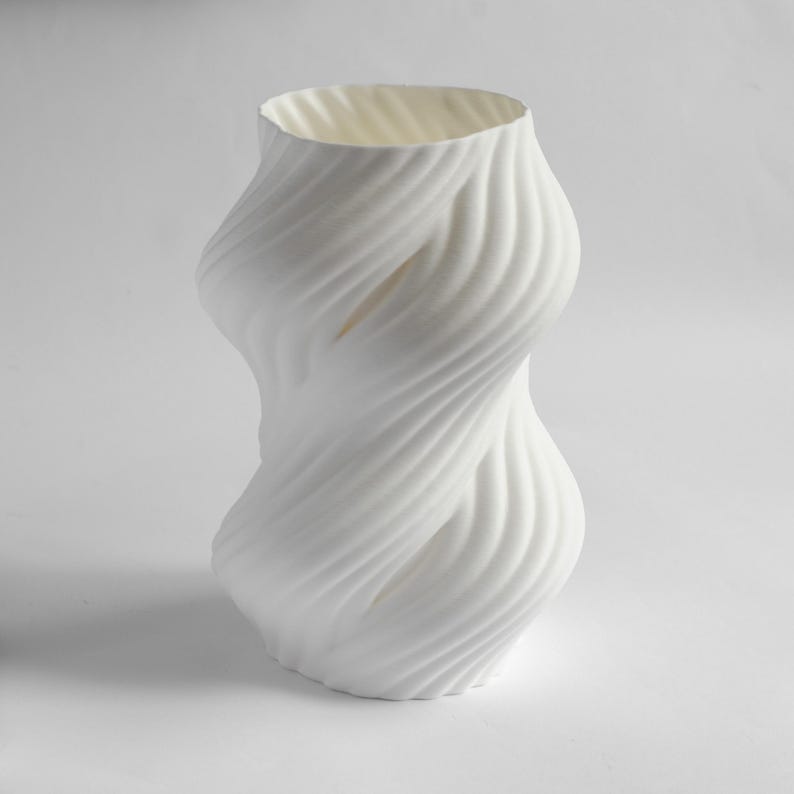 Puede incluir: Un jarr&oacute;n blanco escultural con un dise&ntilde;o retorcido &uacute;nico. El jarr&oacute;n tiene una superficie texturizada con un patr&oacute;n en espiral que envuelve su forma. La abertura es ancha y la forma general es org&aacute;nica y moderna. El jarr&oacute;n est&aacute; hecho de un material s&oacute;lido y opaco.