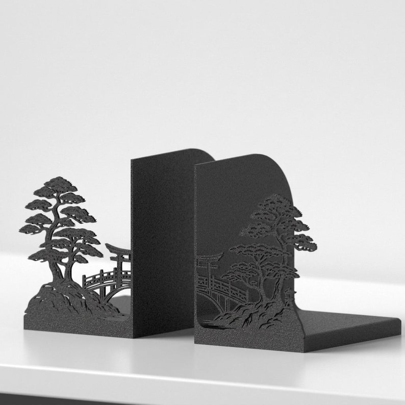Puede incluir: Un par de sujetalibros de metal negro con un dise&ntilde;o de silueta cortado con l&aacute;ser. Cada pieza muestra una escena detallada de un &aacute;rbol, un puente y una puerta torii. El acabado negro mate proporciona un aspecto s&oacute;lido y uniforme a estos soportes.