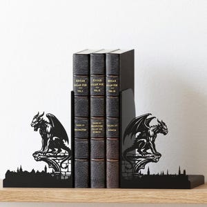 Puede incluir: Soportes de libros de metal negro con un dise&ntilde;o de g&aacute;rgola, que flanquean una fila de tres libros encuadernados en cuero oscuro. Los libros se titulan "Edgar Allan Poe" y "Tales of Imagination, Humor, and Horror."