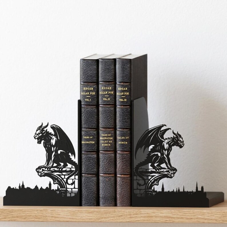 Puede incluir: Soportes de libros de metal negro con un dise&ntilde;o de g&aacute;rgola, que flanquean una fila de tres libros encuadernados en cuero oscuro. Los libros se titulan "Edgar Allan Poe" y "Tales of Imagination, Humor, and Horror."