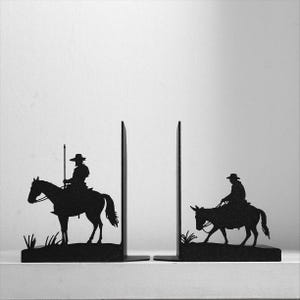 Puede incluir: Un par de sujetalibros de metal negro con siluetas de dos figuras a caballo. El sujetalibros izquierdo muestra a un jinete sosteniendo una lanza larga, mientras que el derecho muestra a un jinete sobre un animal m&aacute;s peque&ntilde;o, sobre un fondo liso.