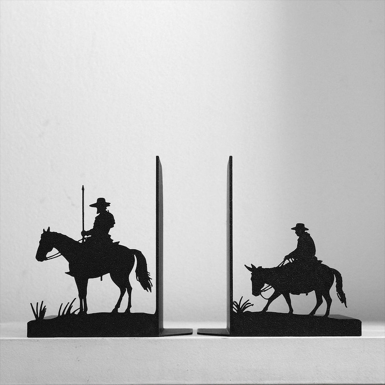 Puede incluir: Un par de sujetalibros de metal negro con siluetas de dos figuras a caballo. El sujetalibros izquierdo muestra a un jinete sosteniendo una lanza larga, mientras que el derecho muestra a un jinete sobre un animal m&aacute;s peque&ntilde;o, sobre un fondo liso.