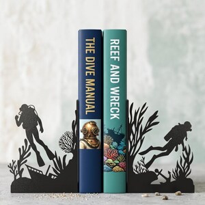 Puede incluir: Un par de sujetalibros de metal negro con siluetas de buceadores, arrecifes de coral y naufragios. Los sujetalibros sostienen dos libros titulados The Dive Manual y Reef and Wreck, que presentan ilustraciones de un casco de buceo y coral.