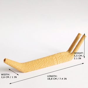 Puede incluir: Un objeto de cer&aacute;mica de color beige claro, alargado, con un patr&oacute;n geom&eacute;trico texturizado. Presenta una abertura en un extremo y dos puntas dirigidas hacia arriba en el otro. Las dimensiones son 18,8 cm de largo, 2,6 cm de ancho y 5,5 cm de alto.
