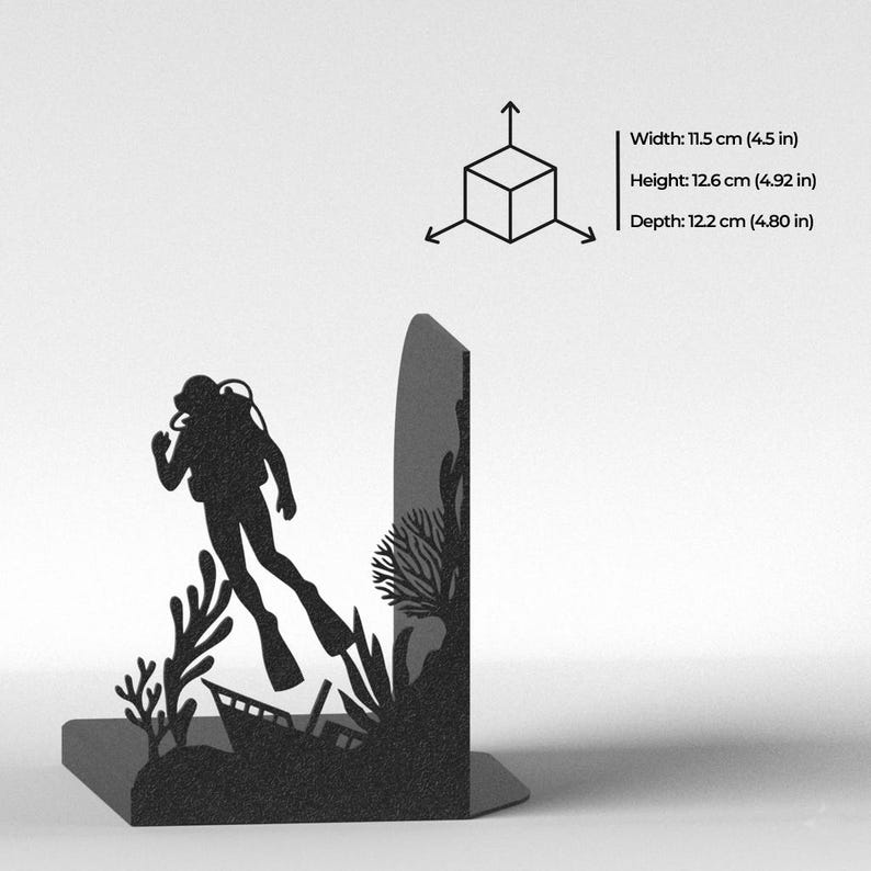 Puede incluir: Un sujetalibros de metal negro con la silueta de un buceador nadando cerca de corales y un naufragio. Las dimensiones son 11,5 cm de ancho, 12,6 cm de alto y 12,2 cm de profundidad, junto a un diagrama de cubo con flechas indicativas.