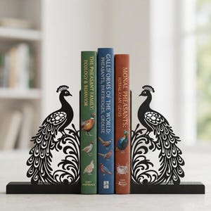 Puede incluir: Un par de sujetalibros de metal negro con la silueta detallada de un pavo real y un diseño de cola ornamentada con volutas. Los sujetalibros sostienen tres libros titulados The Pheasant Family: Ecology & Behavior, Galliforms of the World y Monal Pheasants.