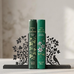Puede incluir: Dos sujetalibros de metal negro con siluetas cortadas con láser de enredaderas y un pequeño pájaro. Los sujetalibros sostienen dos libros de tapa dura verdes titulados Vines & Climbers de Eliza Reed y The Art of Trailing de Julian Bell.