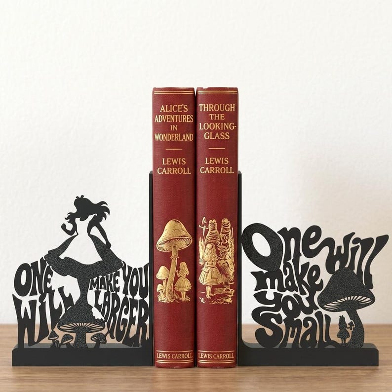 Puede incluir: Dos sujetalibros de metal negro con siluetas de Alicia y setas con el texto One Will Make You Larger y One Will Make You Small, que sostienen dos libros de tapa dura rojos titulados Alice's Adventures in Wonderland y Through the Looking-Glass.