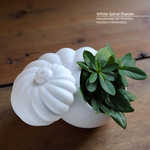 May include: A white, spiral-shaped planter with a lid, holding green plants. The planter is 3D printed and has a modern, minimalist design. Text on the image reads "White Spiral Planter, Handmade 3D Printed, Modern Minimalist."