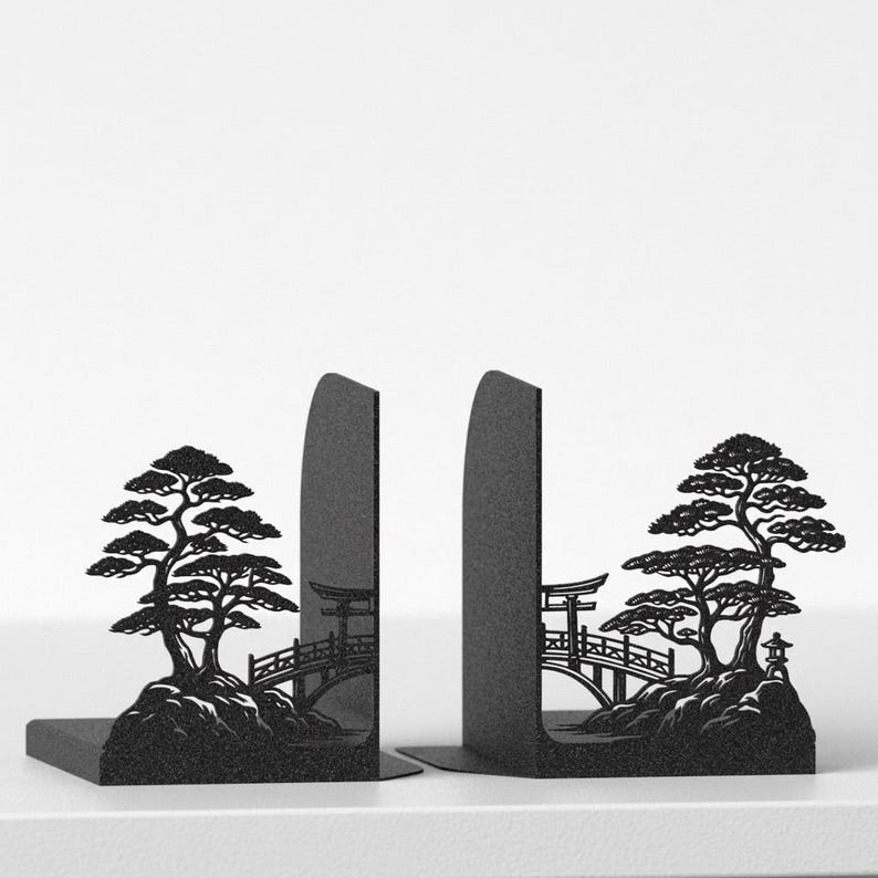 Puede incluir: Un par de sujetalibros de metal negro con un dise&ntilde;o de silueta cortado con l&aacute;ser. Cada pieza representa un paisaje detallado con un puente curvo, una puerta torii, una linterna de piedra y un pino sobre una base rocosa texturizada.
