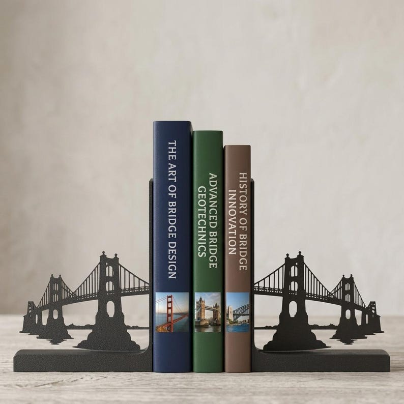 May include: A pair of black metal bookends featuring a bridge silhouette design, holding three books titled The Art of Bridge Design, Advanced Bridge Geotechnics, and History of Bridge Innovation, each with a small photographic bridge image.