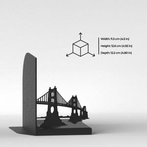 May include: A black metal bookend featuring a silhouette of a suspension bridge. The dimensions are printed as Width: 11.5 cm (4.5 in), Height: 12.6 cm (4.92 in), and Depth: 12.2 cm (4.80 in), accompanied by a 3D cube icon with directional arrows.