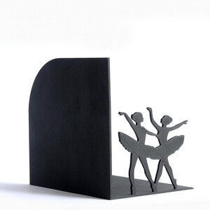 May include: Black bookend featuring a silhouette of two ballerinas in graceful poses. The bookend has a solid black, curved back and a base for stability. The dancers are detailed with tutus and arms raised, perfect for a ballet enthusiast.