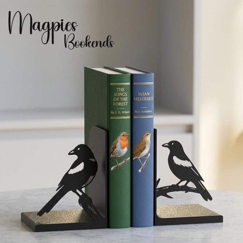 Puede incluir: Un par de sujetalibros de metal negro con siluetas de urracas posadas en ramas. Los sujetalibros sostienen dos libros de tapa dura titulados The Songs of the Forest y Avian Melodies, que presentan ilustraciones de aves en sus lomos.