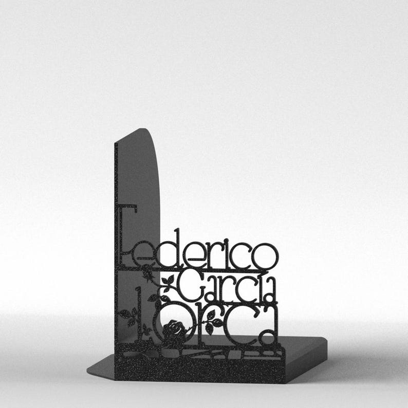 May include: Black metal bookend featuring the name "Federico Garcia Lorca" in a decorative font. The design includes floral accents and a rectangular base, suitable for holding books. The bookend is set against a white background.