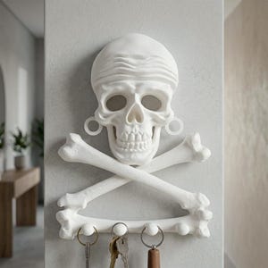 Puede incluir: Un soporte de pared blanco para llaves con forma de cr&aacute;neo humano que lleva un pa&ntilde;uelo, con huesos cruzados debajo. El cr&aacute;neo presenta dilatadores circulares en las orejas y cuatro ganchos peque&ntilde;os en la base, tres de ellos con llaves.