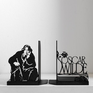 Puede incluir: Un par de sujetalibros de metal negro. Uno muestra la silueta de una persona con el pelo largo sosteniendo un bast&oacute;n, mientras que el otro presenta el texto OSCAR WILDE integrado en un dise&ntilde;o floral decorativo con l&iacute;neas curvas y hojas.