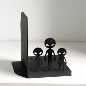 Puede incluir: Sujetalibros negros con forma de familia alien&iacute;gena. Los sujetalibros presentan tres figuras de alien&iacute;genas estilizadas sobre una base rectangular. Fabricados en material negro, est&aacute;n dise&ntilde;ados para mantener los libros en posici&oacute;n vertical.