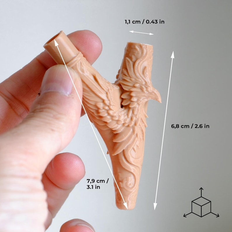 Op de afbeelding: Een beige, Y-vormig object met een gedetailleerd feniksontwerp. Het object is 7,9 cm lang, 6,8 cm hoog en 1,1 cm breed. De feniks heeft uitgespreide vleugels en is in het oppervlak gesneden. Het object wordt door een hand vastgehouden.