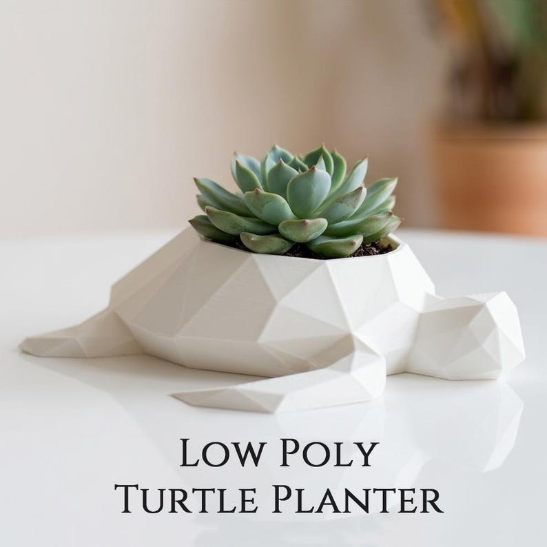 Puede incluir: Una maceta de tortuga blanca de baja poli, con una planta suculenta. El dise&ntilde;o geom&eacute;trico de la tortuga es moderno y minimalista. El texto "LOW POLY TURTLE PLANTER" se muestra debajo.