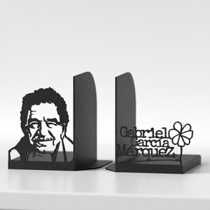 Puede incluir: Un par de sujetalibros de metal negro que presentan un retrato en silueta de Gabriel Garc&iacute;a M&aacute;rquez en una pieza y el texto "Gabriel Garc&iacute;a M&aacute;rquez" junto a una flor estilizada en la otra, ambos con un acabado mate.